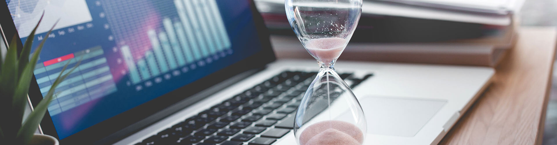 Hourglass standing on top of laptop with financial market graphs on screen